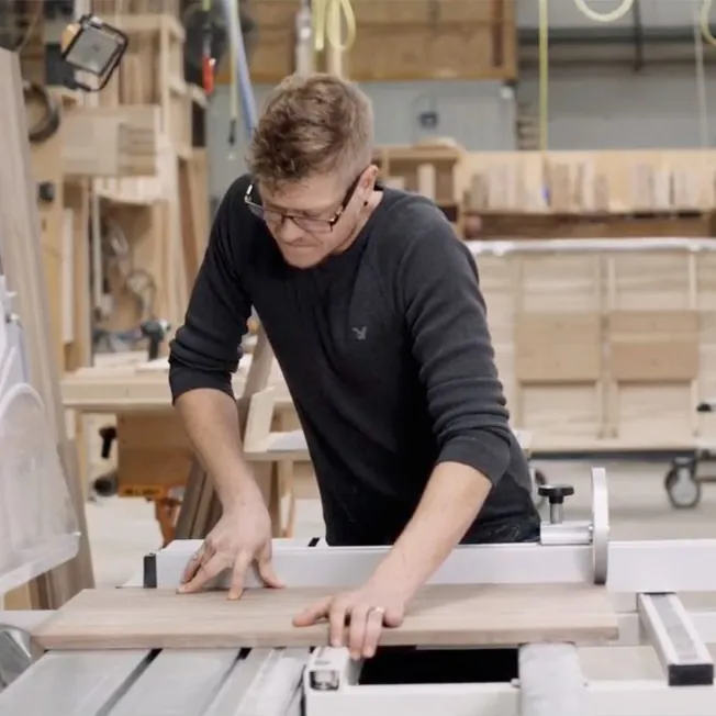 A craftsman cutting a hardwood board in a Canadian furniture workshop